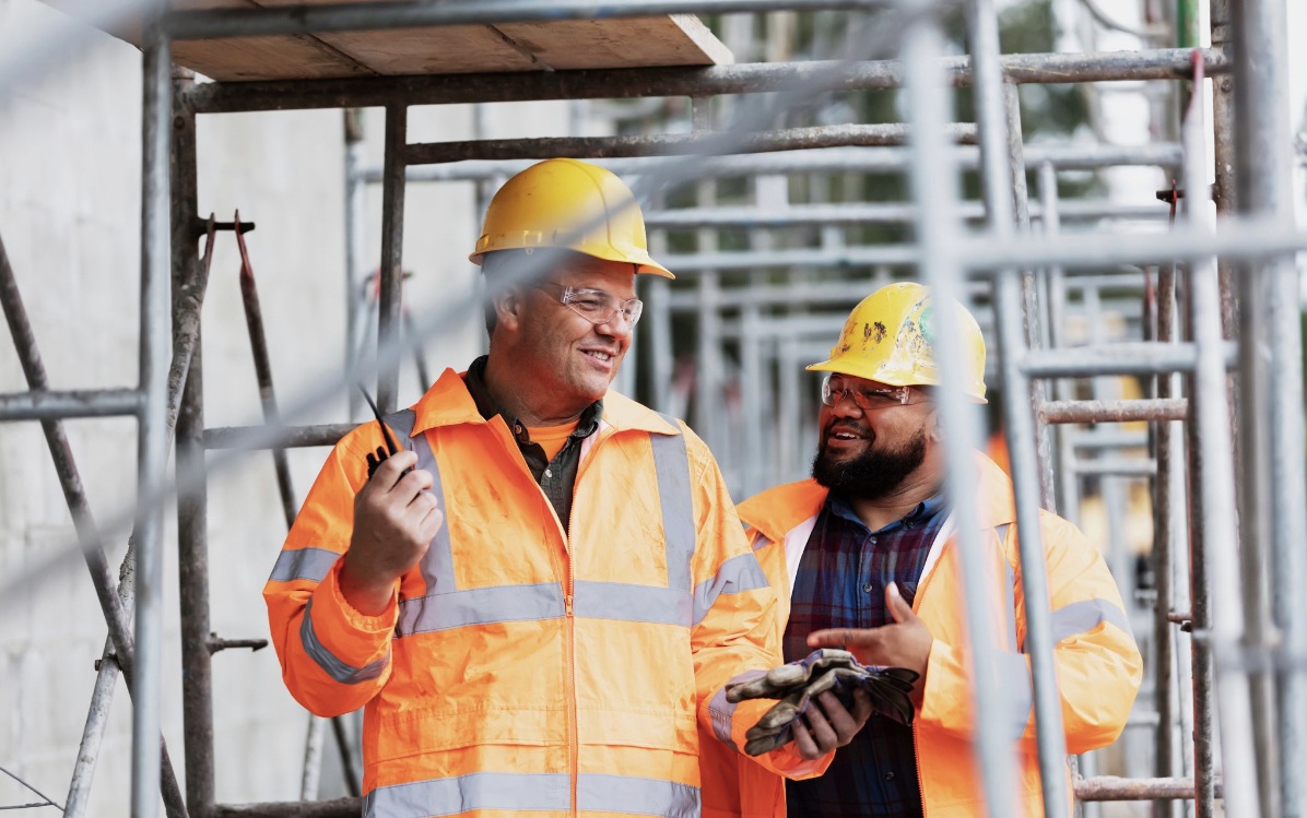Two construction workers in hi-vis talking together on a scaffolded site